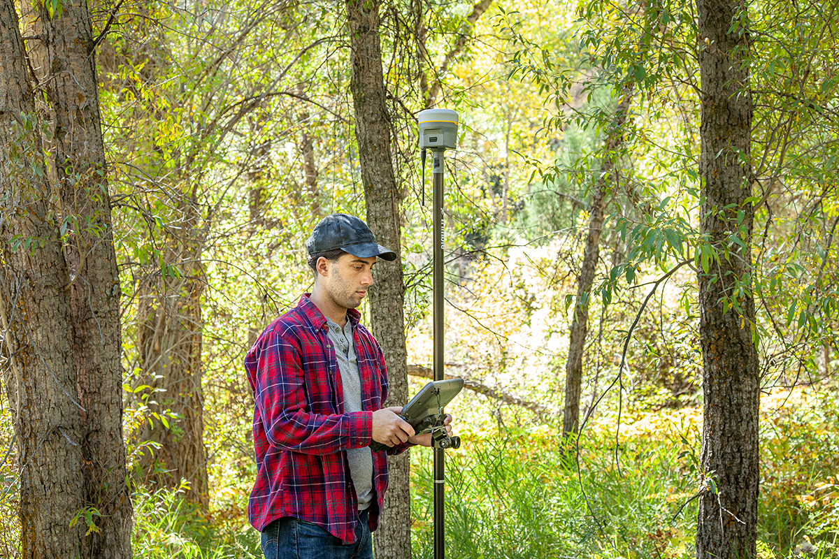 Trimble R12 Man surveying under trees with a survey GNSS rover