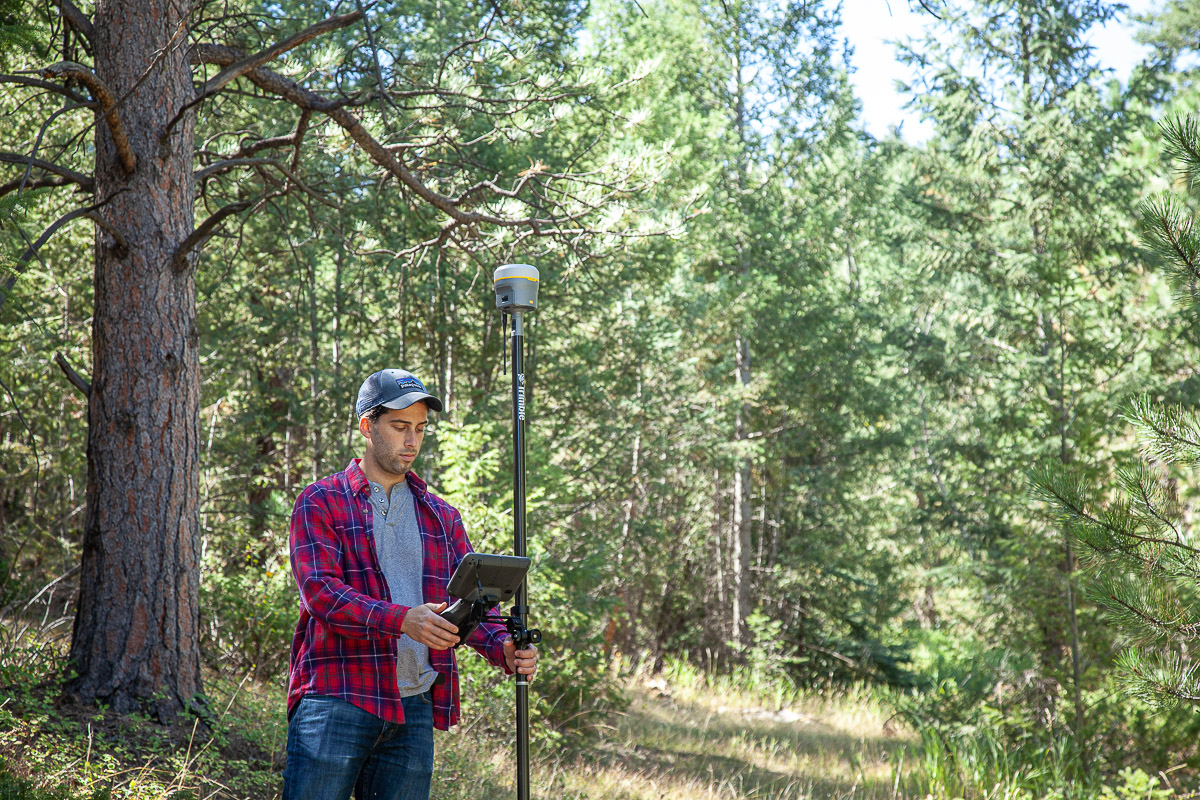 Trimble R12 Man standing in a pine forest with a survey GNSS rover unit